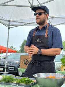 a man wearing an apron standing in front of a table full of food