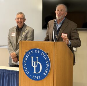 two men standing at a podium in front of a projector screen