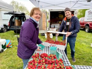 a couple of people standing next to a table full of strawberries