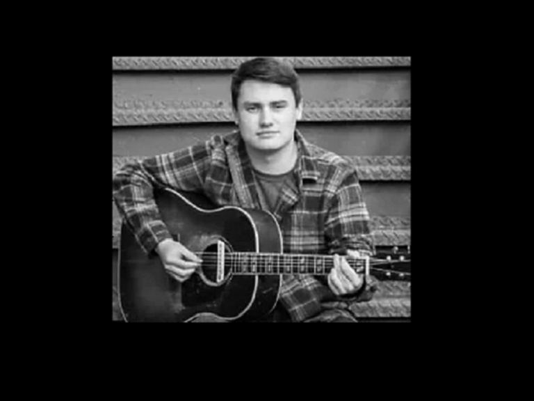 a man playing an acoustic guitar in front of stairs